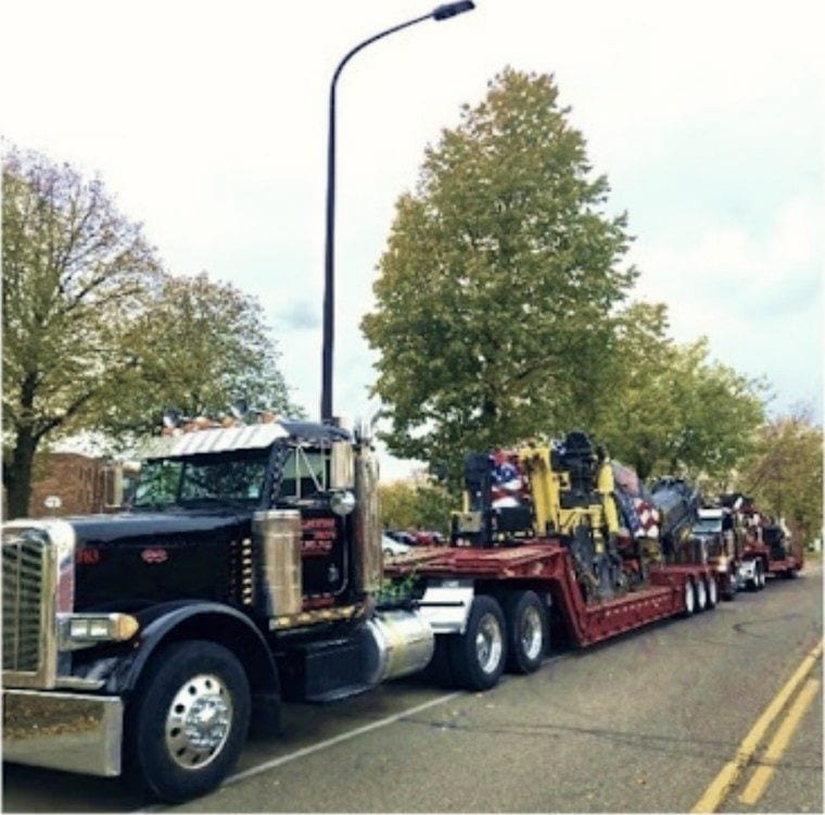 The lowboy loaded with equipment, waiting at the curb.