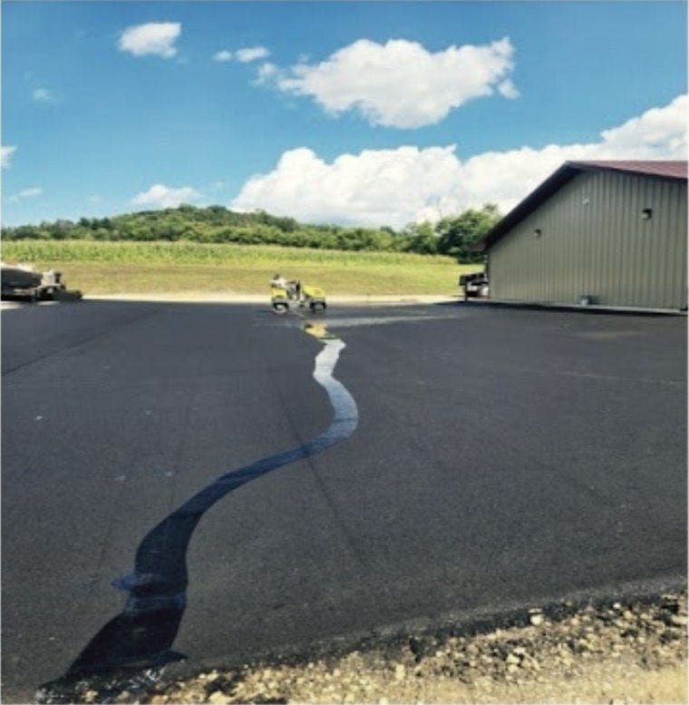 A wide new drive up to an outbuilding, the edge still crisp against raw ground.