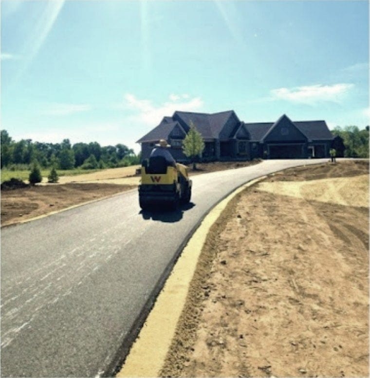 The roller running out a new drive toward a big house under a clear sky.